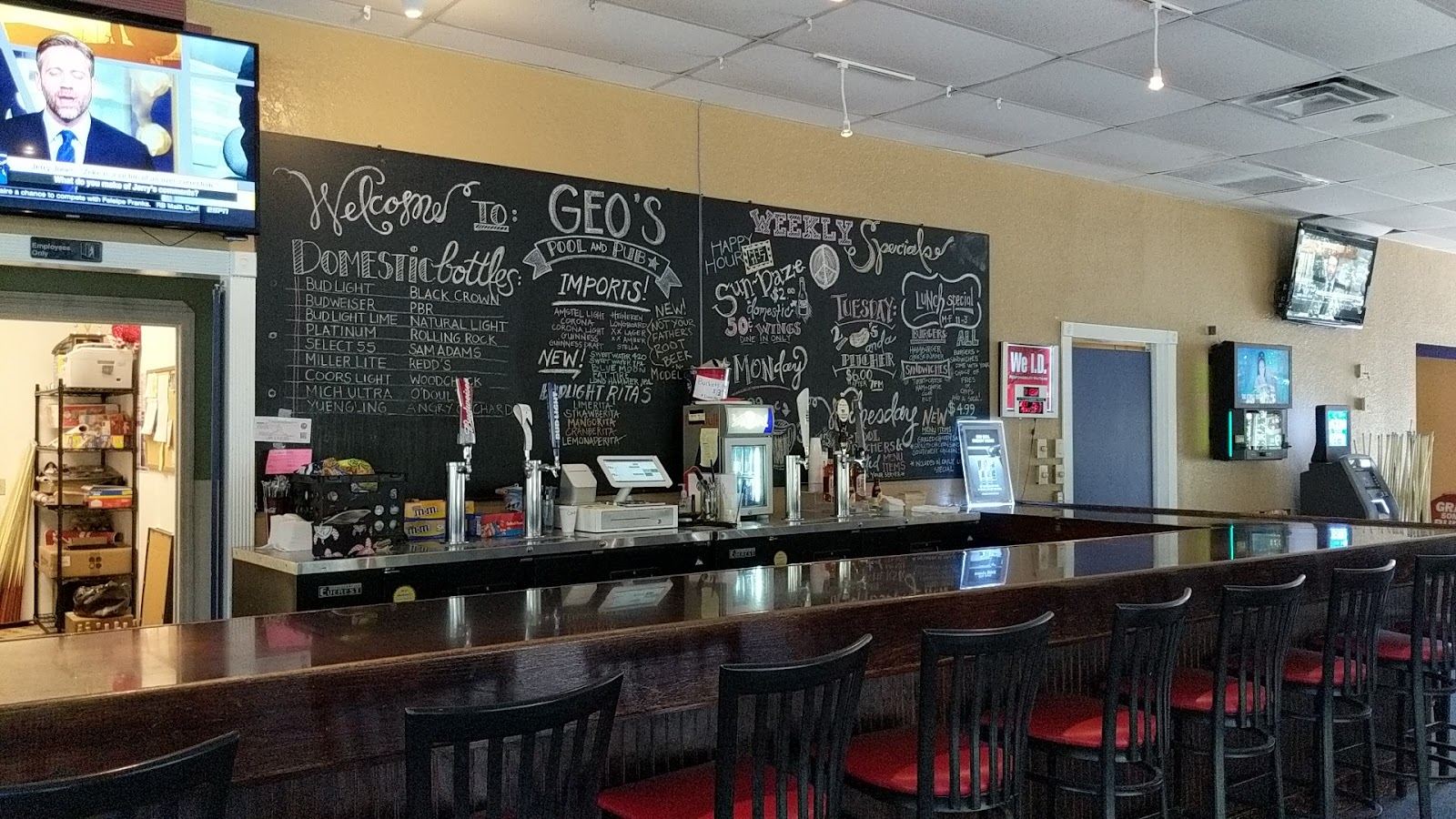 The long wooden bar with red stools, under a black chalkboard wall hand lettered with the beer list and the weekly specials.
