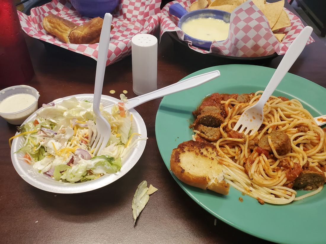 A plate of spaghetti with sauce and garlic bread, a side salad, and a bowl of queso with tortilla chips.